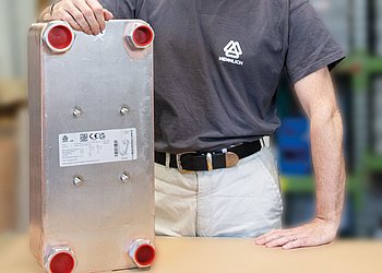 Auf einem Tisch steht ein Plattenwärmetauscher, dahinter steht ein Mitarbeiter in Hennlich Shirt